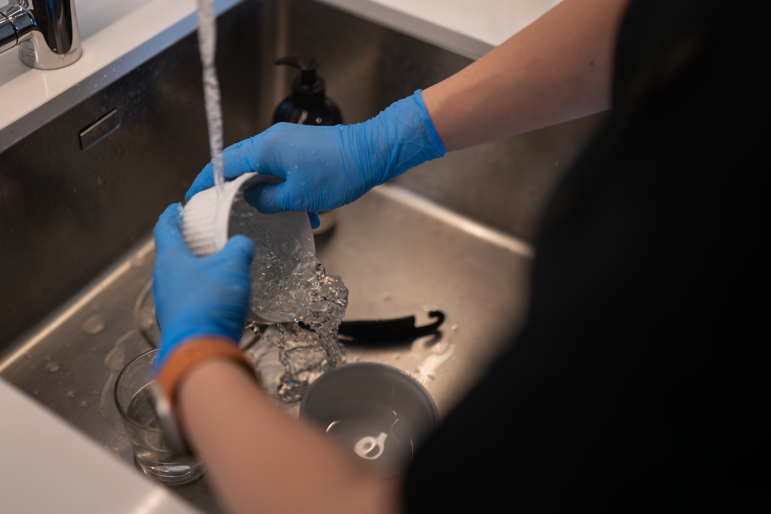 Gloved hands washing up at a kitchen sink